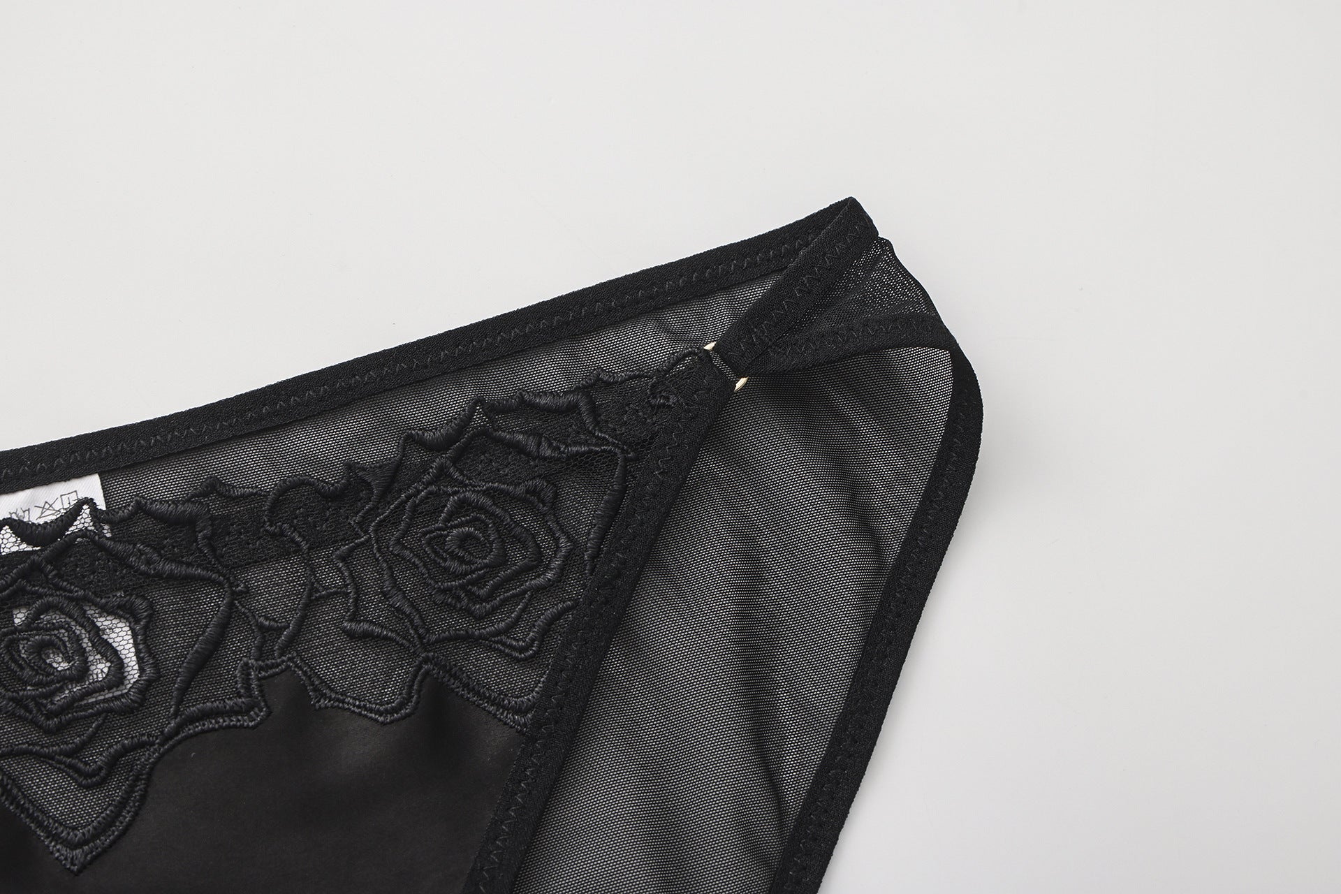 Close-up of 3D tactile rose embroidery on sheer black mesh fabric.