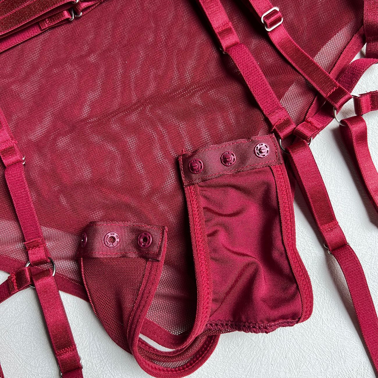 A detailed close-up of the functional snap closure at the base of the burgundy sheer mesh bodysuit, showcasing the clean finish and soft-touch fabric.
