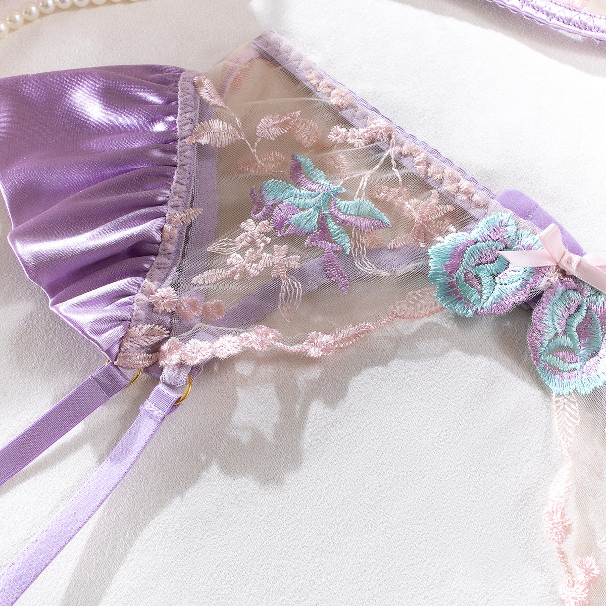 Close-up of the Dawn Whisper garter belt. Featuring the soft satin ruffles and the gold-tone clips designed to hold Linework Collection stockings.