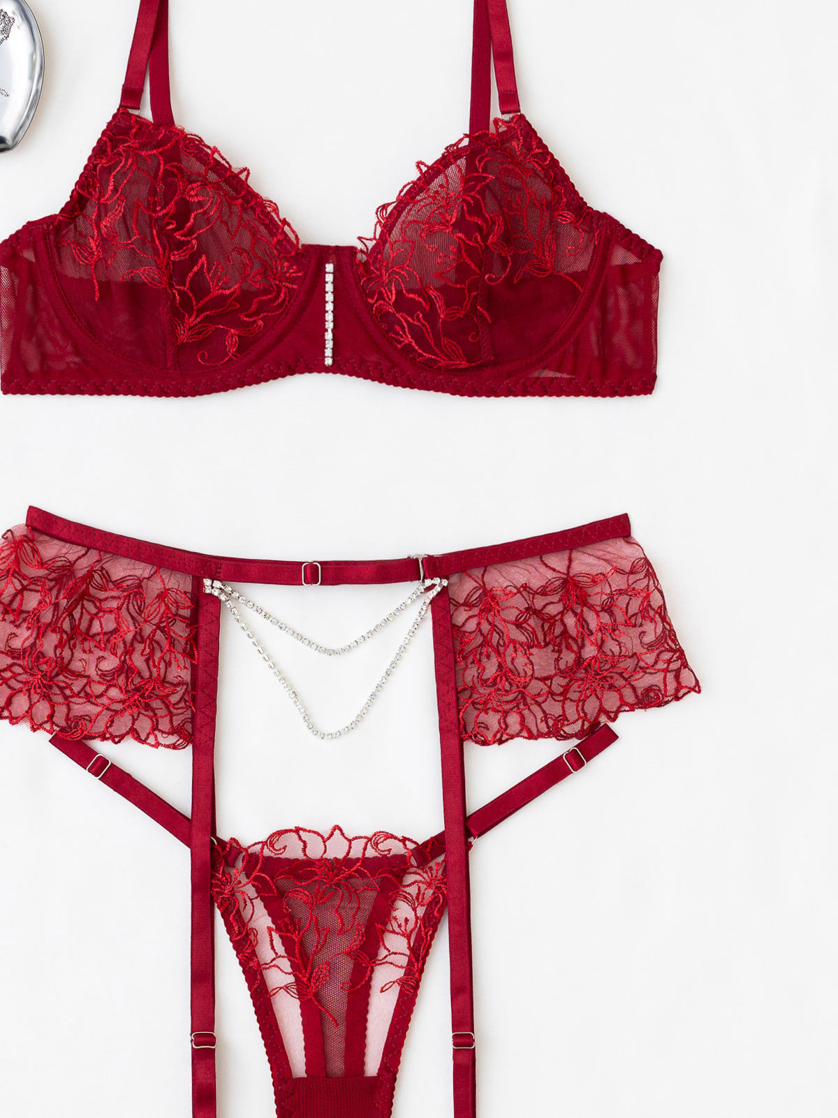 Studio flat lay of the 3-piece burgundy set on a white background, featuring the embroidered underwire bra, thong, and pearl garter.