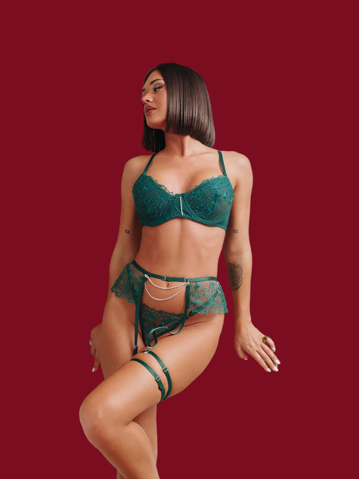 High-fashion editorial shot of the emerald green embroidered set; the model features a dynamic pose with one leg raised to showcase the high-recovery stretch of the garter and the jewelry-inspired pearl chain against the deep jewel-toned mesh.