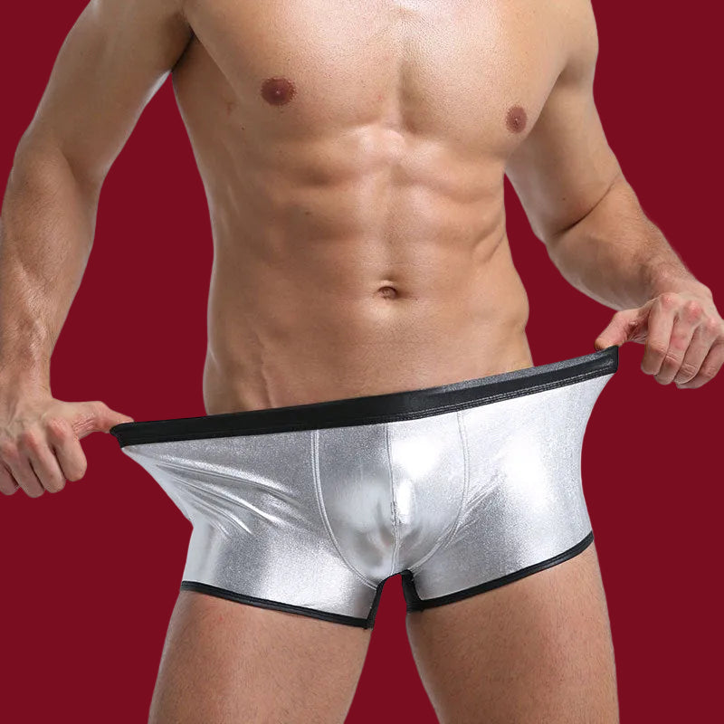 Silver metallic boxer briefs reflecting a high-contrast liquid sheen against a deep burgundy backdrop.
