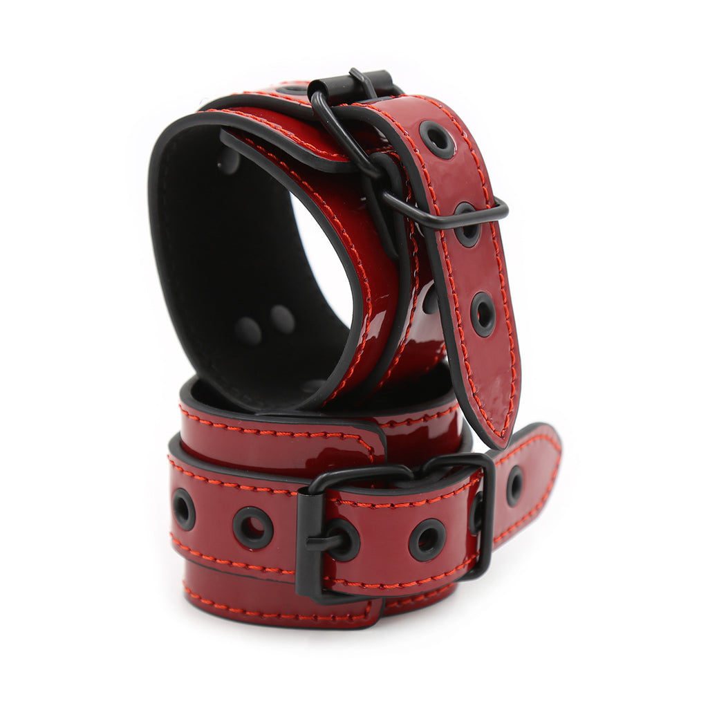 Close-up of two pairs of high-gloss red patent leather adjustable cuffs with reinforced silver hardware.