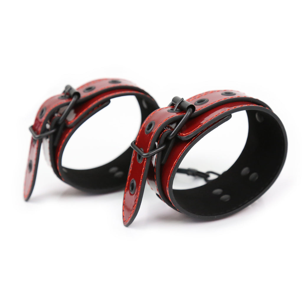 A pair of high-gloss red patent leather ankle cuffs stacked to show the reinforced black hardware and adjustable strap design.