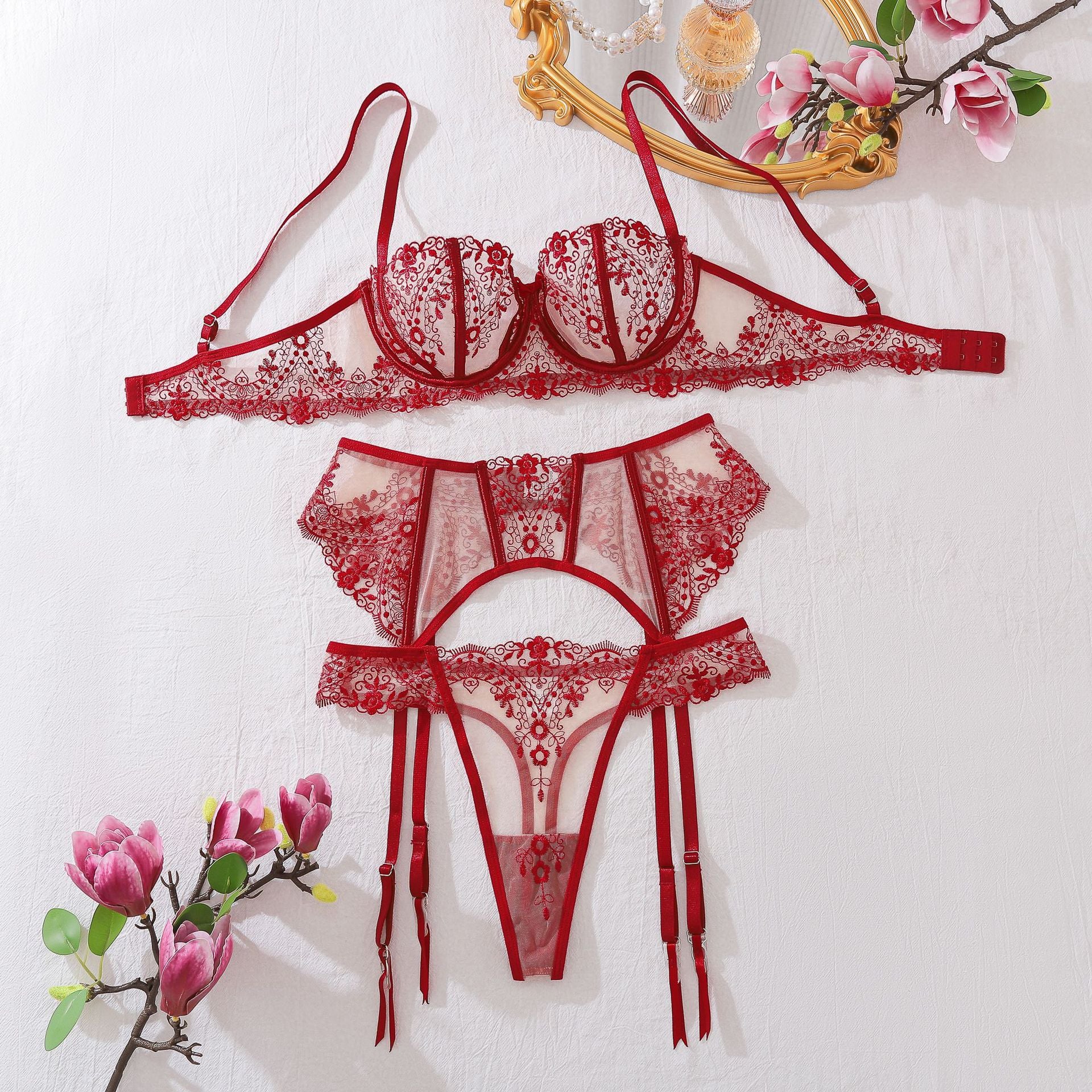 A complete front-view flat lay of the 3-piece set. The image showcases the symmetry of the floral embroidery and the architectural layout of the balcony bra, garter, and thong.